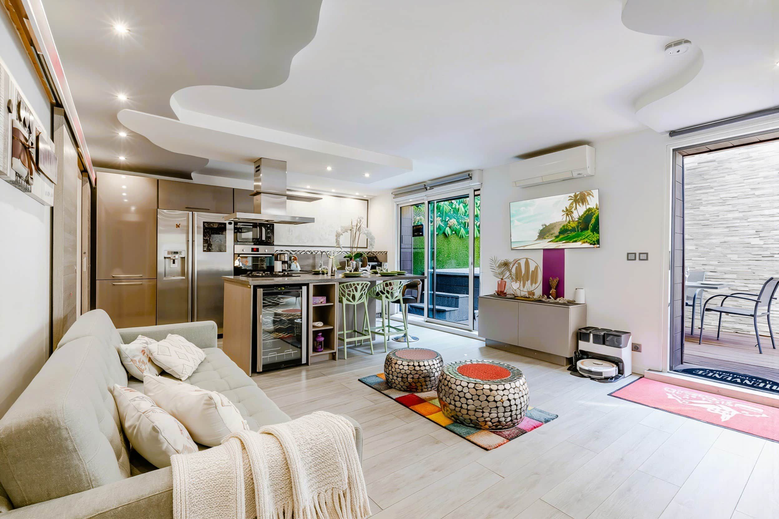 En moderne stue med sofa, spiseområde med stole, køkken med hårde hvidevarer og en balkon med udsigt.