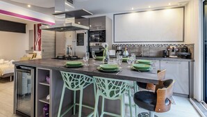 Een moderne keuken met een centraal eiland, barkrukken, een inbouwoven en een groot raam.