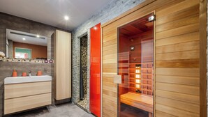 Een moderne badkamer met een wastafel, douchegedeelte en een houten sauna.