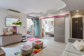 A modern living room with a sofa, ottomans, a TV, and a dining area with a table and chairs. - Gites Spa Strasbourg Appartement le 14 jacuzzi sauna privé, Gite le 14 (Furdenheim)