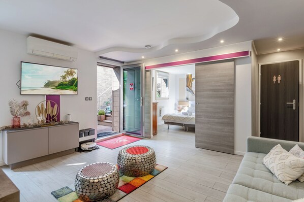 A modern living room with a sofa, ottomans, a TV, and a dining area with a table and chairs.