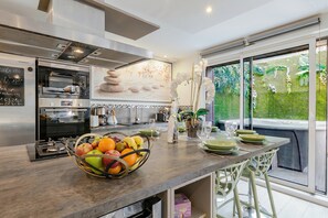 Eine moderne Küche mit einer großen Kochinsel, einem eingebauten Backofen und Blick auf einen Garten durch eine Schiebetür.