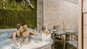 Een bubbelbad met een koppel, een tafel met stoelen en een bakstenen muur begroeid met groen.