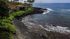 A coastal area with a rocky shoreline, lush greenery, and a clear blue sky. - KKSR#7303 Remodeled Top Floor Unit With Loft, Golf Course Views (Kailua Kona)