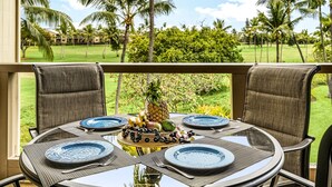 A table set for four with a tropical fruit centerpiece, overlooking a lush garden with palm trees. - KKSR#7303 Remodeled Top Floor Unit With Loft, Golf Course Views (Kailua Kona)
