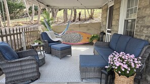 Une terrasse couverte avec des meubles en osier, un hamac et une planche de surf.