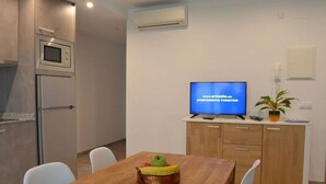 A modern kitchen with a microwave and refrigerator, a dining table with chairs, a television displaying a website, and a potted plant. - 1.2 NEW in center ROSES with WI-FI, AC and TV sat at 60 m MAR (Roses)