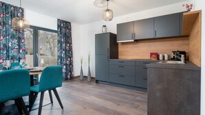 A modern kitchen with grey cabinets, a wooden countertop, and a dining area with teal chairs.