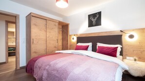 A bedroom with a large bed, wooden wardrobe, and a headboard with wall-mounted lights.