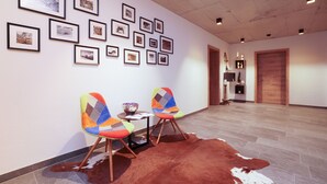 A hallway with framed pictures on the wall, two colorful chairs, a small table, and a cowhide rug.
