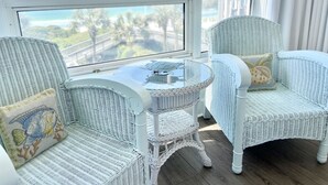 A room with wicker furniture, a round table, and a view of a bridge and greenery.