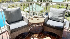 A balcony with wicker furniture, a small round table, and a view of the ocean.
