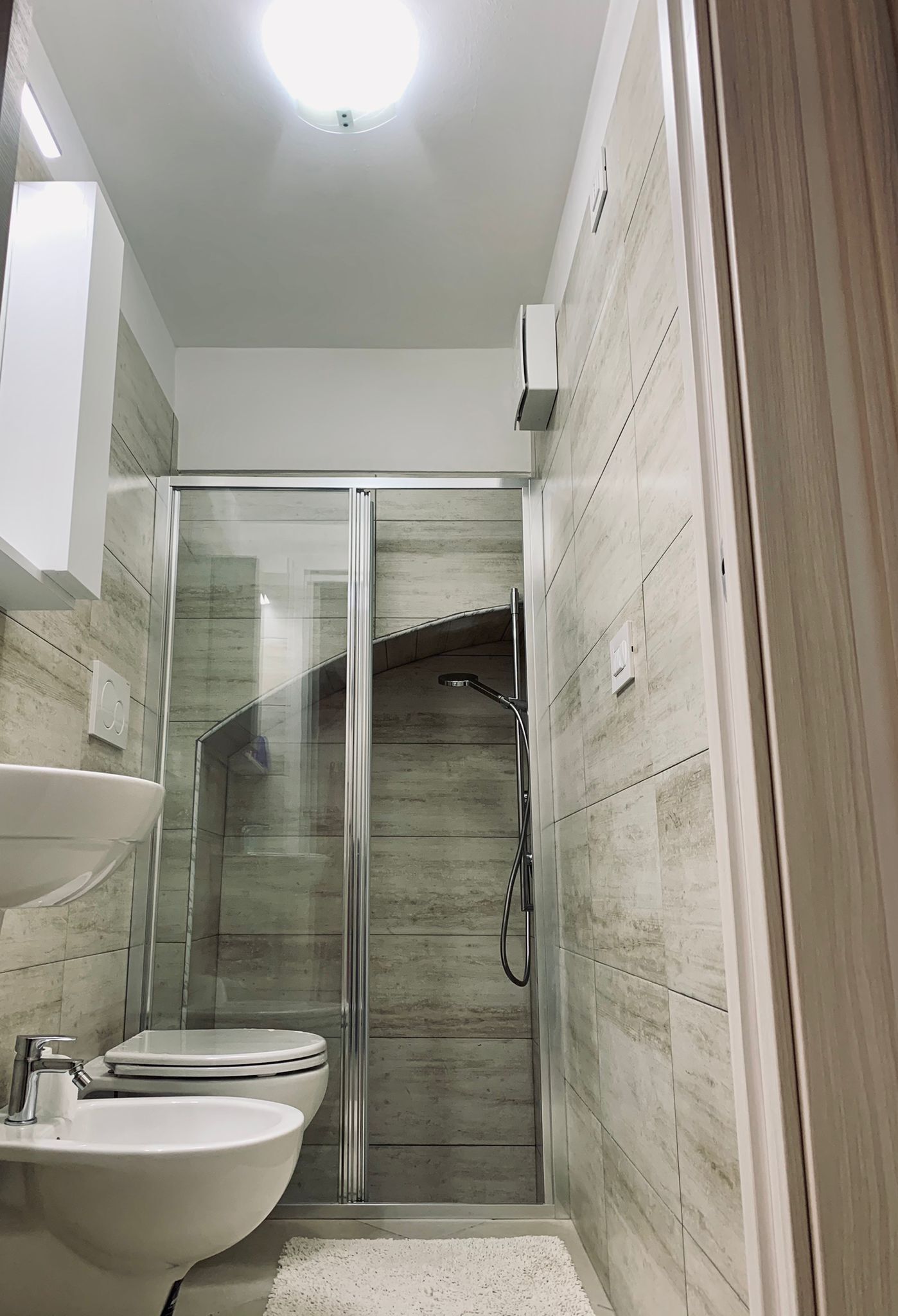 Ein modernes Badezimmer mit einer Duschkabine, einem weißen Waschbecken und einer Toilette.