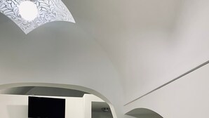 A modern room with a wooden dining table, white chairs, a flat-screen TV mounted on the wall, and a brown sofa. - Dimora Sportelli (Polignano a Mare)