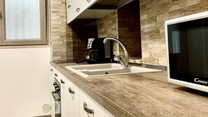 A modern kitchen with white cabinets, a wooden countertop, a built-in microwave, and a window above the sink. - Dimora Sportelli (Polignano a Mare)