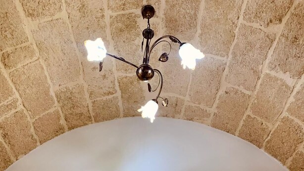 A bedroom with a stone wall, a tufted headboard, and a chandelier. - Dimora Sportelli (Polignano a Mare)