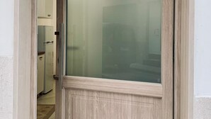 A wooden door with a frosted glass panel, leading into a kitchen with white cabinets and a refrigerator. - Dimora Sportelli (Polignano a Mare)