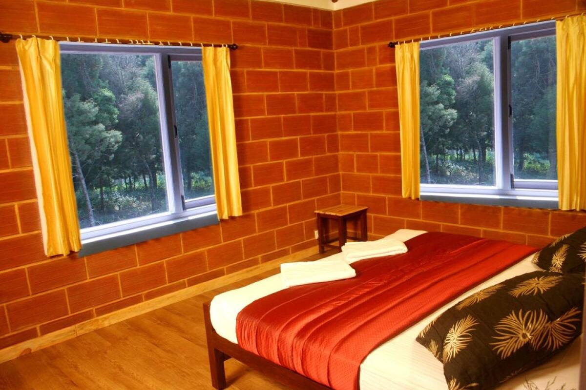 A bedroom with two windows, a bed with a red and white bedspread, and a small wooden stool.