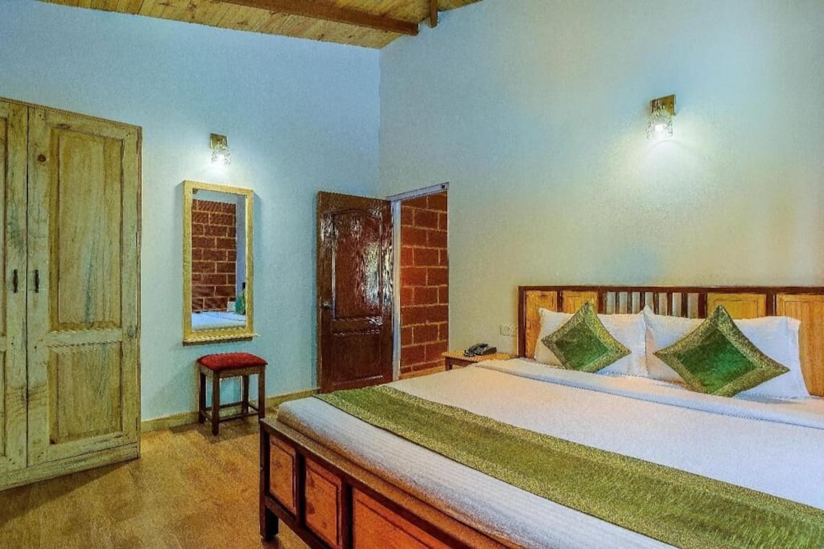 A bedroom with a bed, a wooden wardrobe, a small stool, and a door.