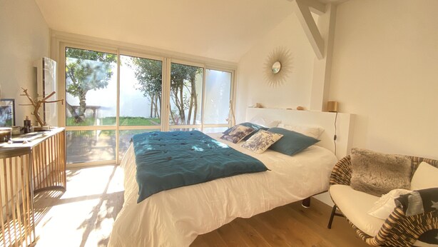 A bedroom with a large bed, a chair, a desk, and a view of the outdoors. - Cocooning villa in a quiet neighborhood near downtown La Teste (La Teste-de-Buch)