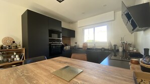 A modern kitchen with a wooden dining table, built-in appliances, and a large window providing natural light. - Cocooning villa in a quiet neighborhood near downtown La Teste (La Teste-de-Buch)