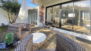 A patio with wicker furniture, a barbecue grill, and a glass door leading to a dining area. - Cocooning villa in a quiet neighborhood near downtown La Teste (La Teste-de-Buch)