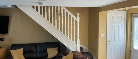 A living room with a black leather sofa, a brown leather sofa, a white staircase, and a white door.