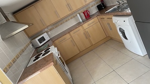 Una cocina compacta con armarios de madera, un microondas, un hervidor y una lavadora.