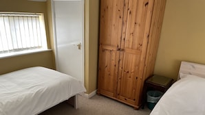 Un dormitorio con dos camas individuales, un armario de madera, una mesita de noche pequeña y una ventana con persianas.