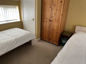 A bedroom with two single beds, a wooden wardrobe, a small bedside table, and a window with blinds. - Sweetpea Cottage - Sleeps 5, Parking & Pets Ok (Louth)