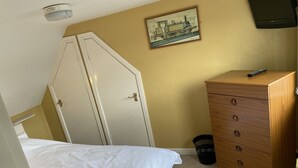 Ett sovrum med en säng, en byrå i trä, en dörr, en tavla och en taklampa.
