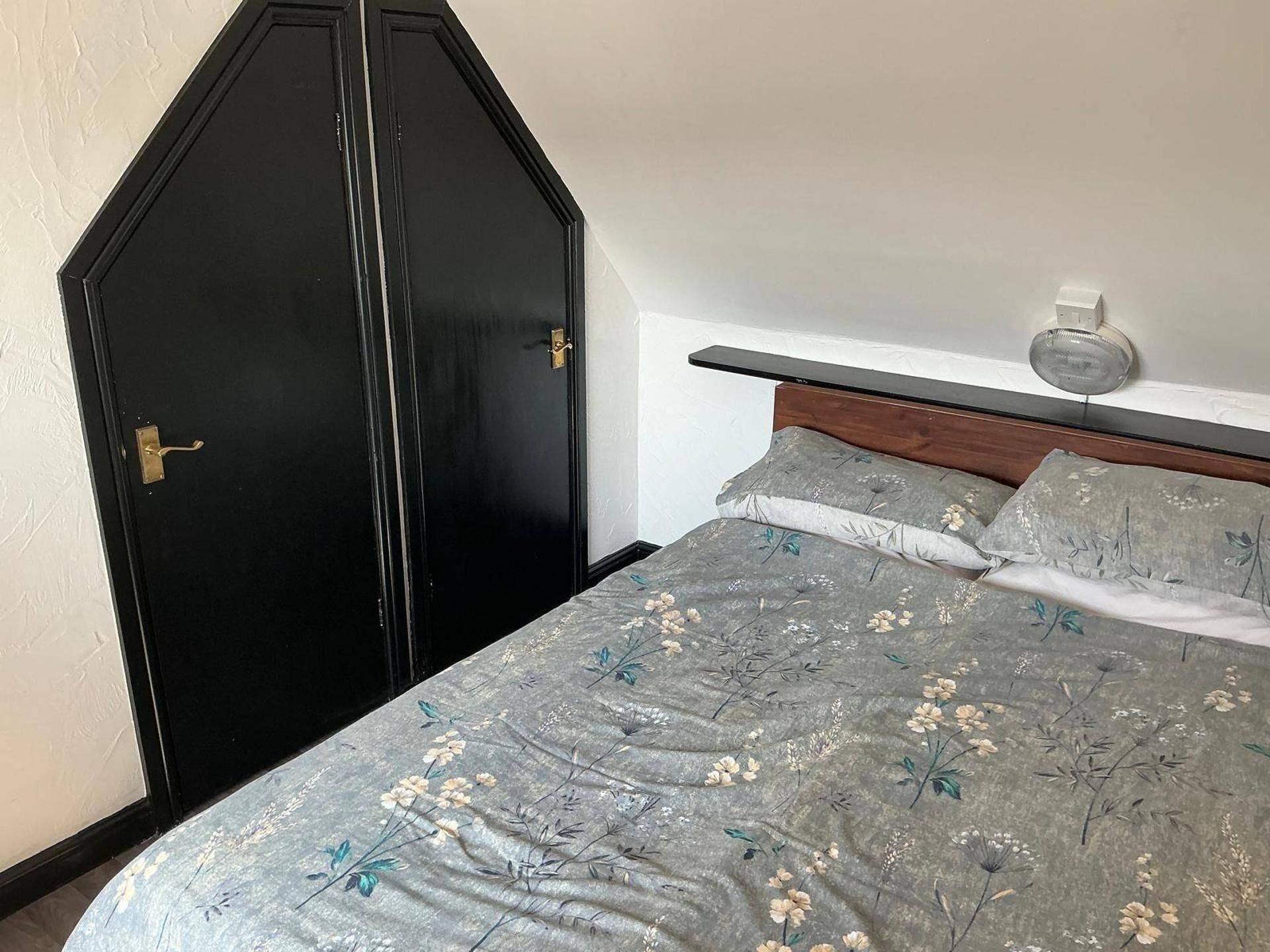 A bedroom with a bed, a nightstand, a wall-mounted light, and a black wardrobe.