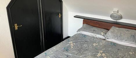 A bedroom with a bed, a nightstand, a wall-mounted light, and a black wardrobe.