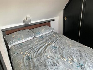 A bed with a floral patterned bedspread, a bedside table with a lamp, and a black wardrobe. - Rain Hill Cottage - Sleeps 4, Parking & Pets Ok (Louth)