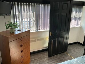 A room with a wooden dresser, a potted plant, a window with blinds, a black door, and a radiator. - Rain Hill Cottage - Sleeps 4, Parking & Pets Ok (Louth)
