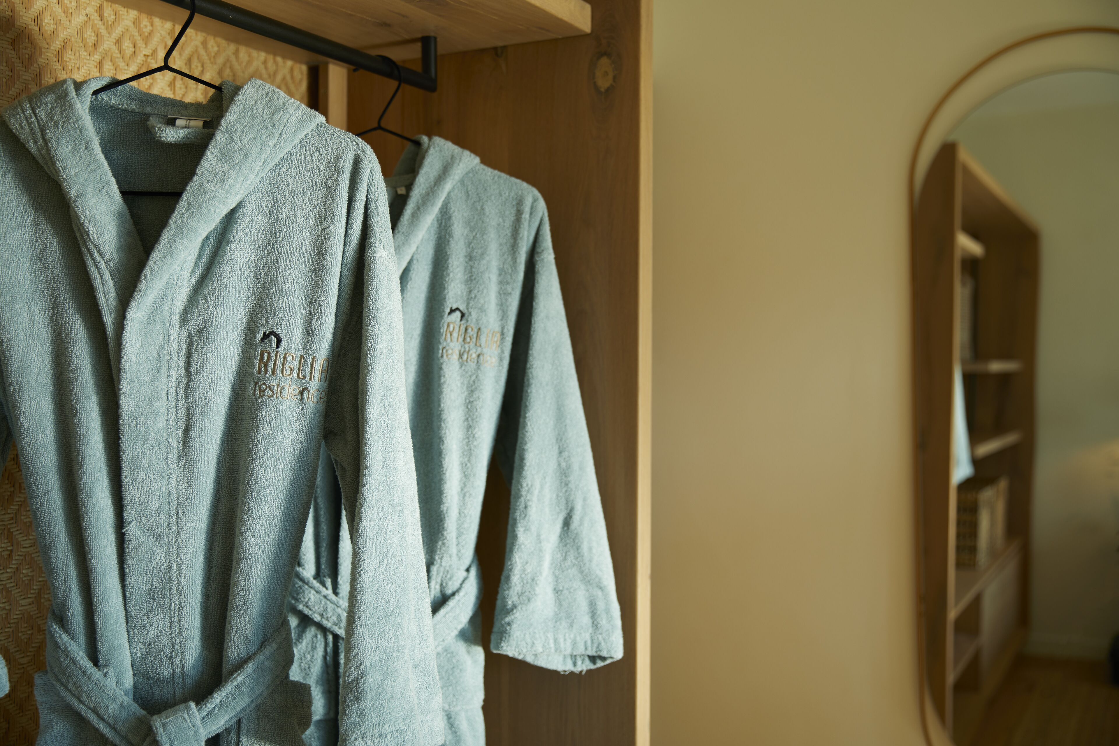 Deux robes bleu clair sont suspendues à un portant en bois dans une pièce dotée d’une porte en bois et d’une bibliothèque.