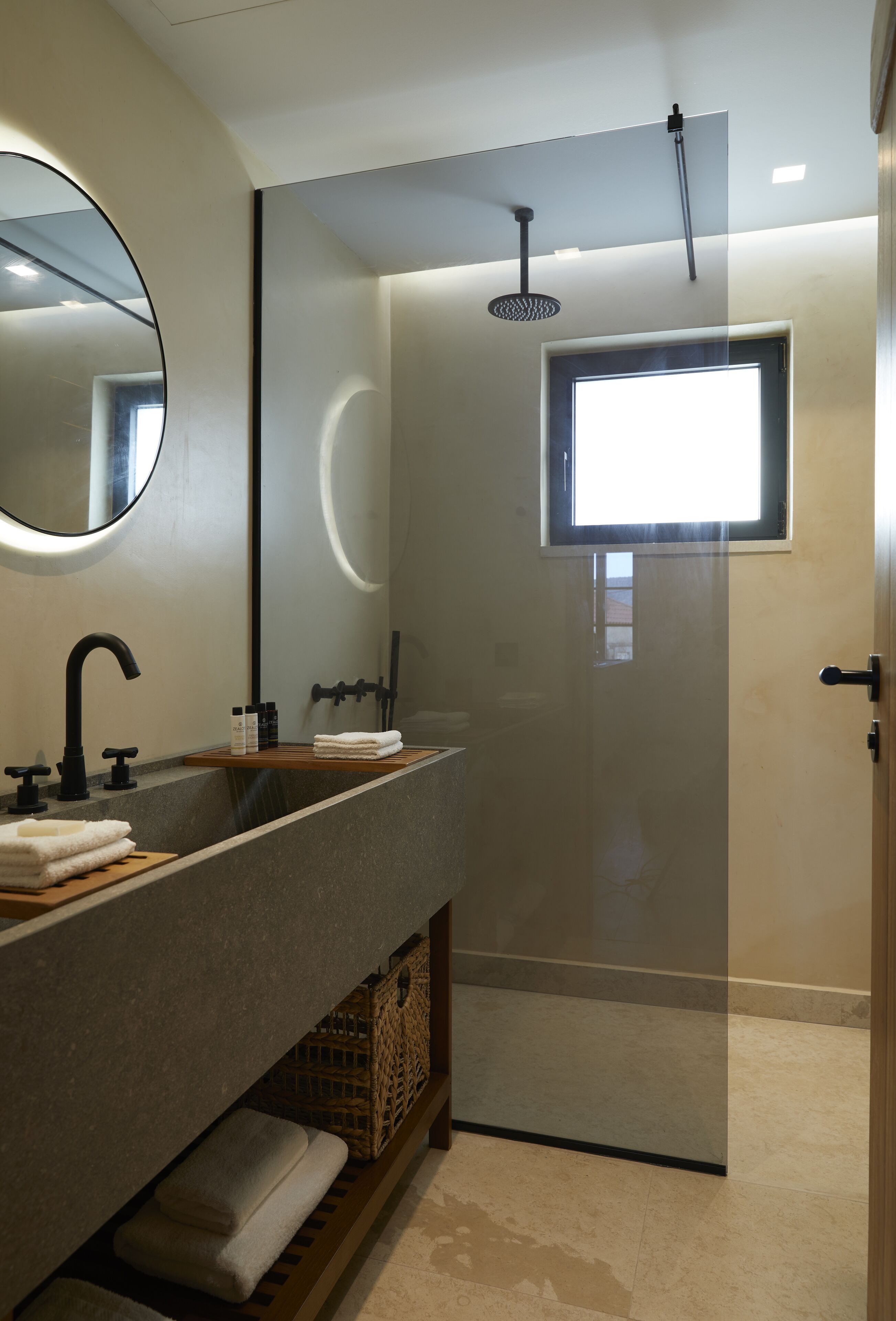 A modern bathroom with a large mirror, a sink with a wooden vanity, a shower with a glass door, and a small window.