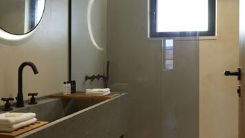 A modern bathroom with a large mirror, a sink with a wooden vanity, a shower with a glass door, and a small window.