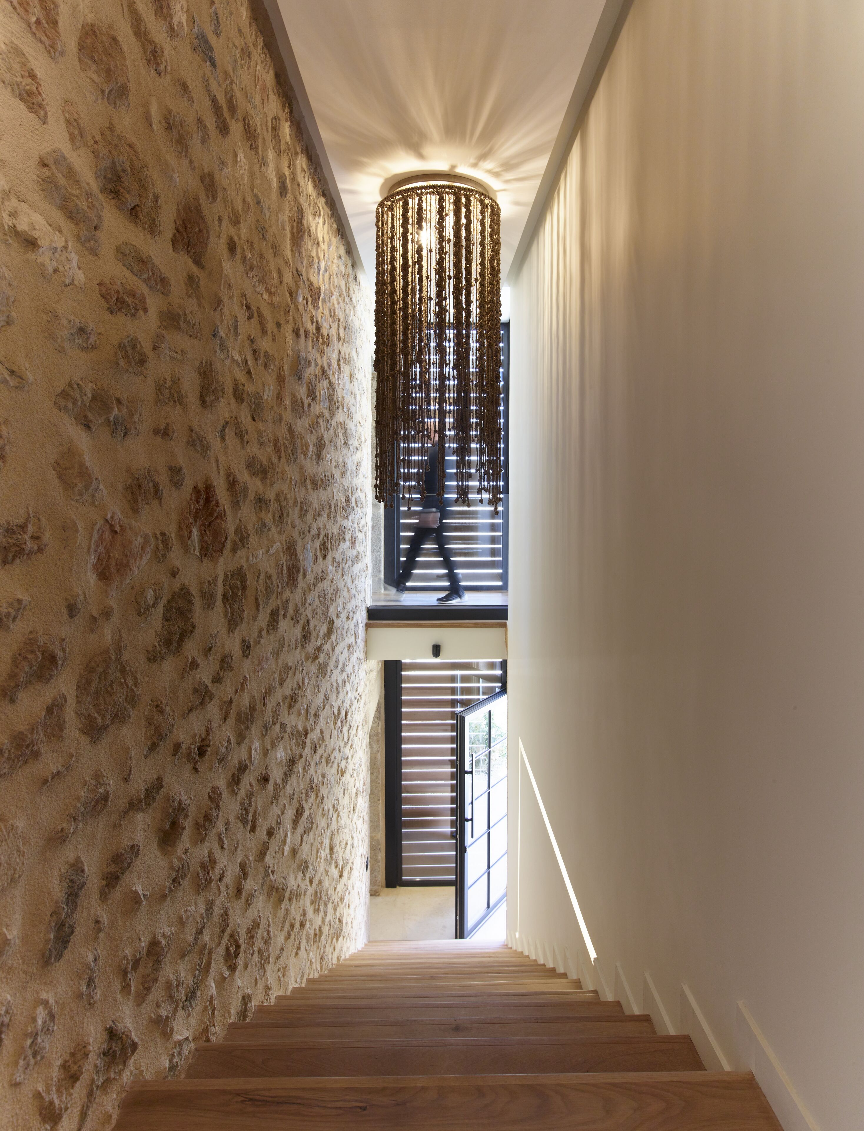 Una escalera con un pared texturizado a un lado y un accesorio de luz moderno en la parte superior.