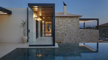 A modern house with a swimming pool, stone walls, and a glass-enclosed entrance.