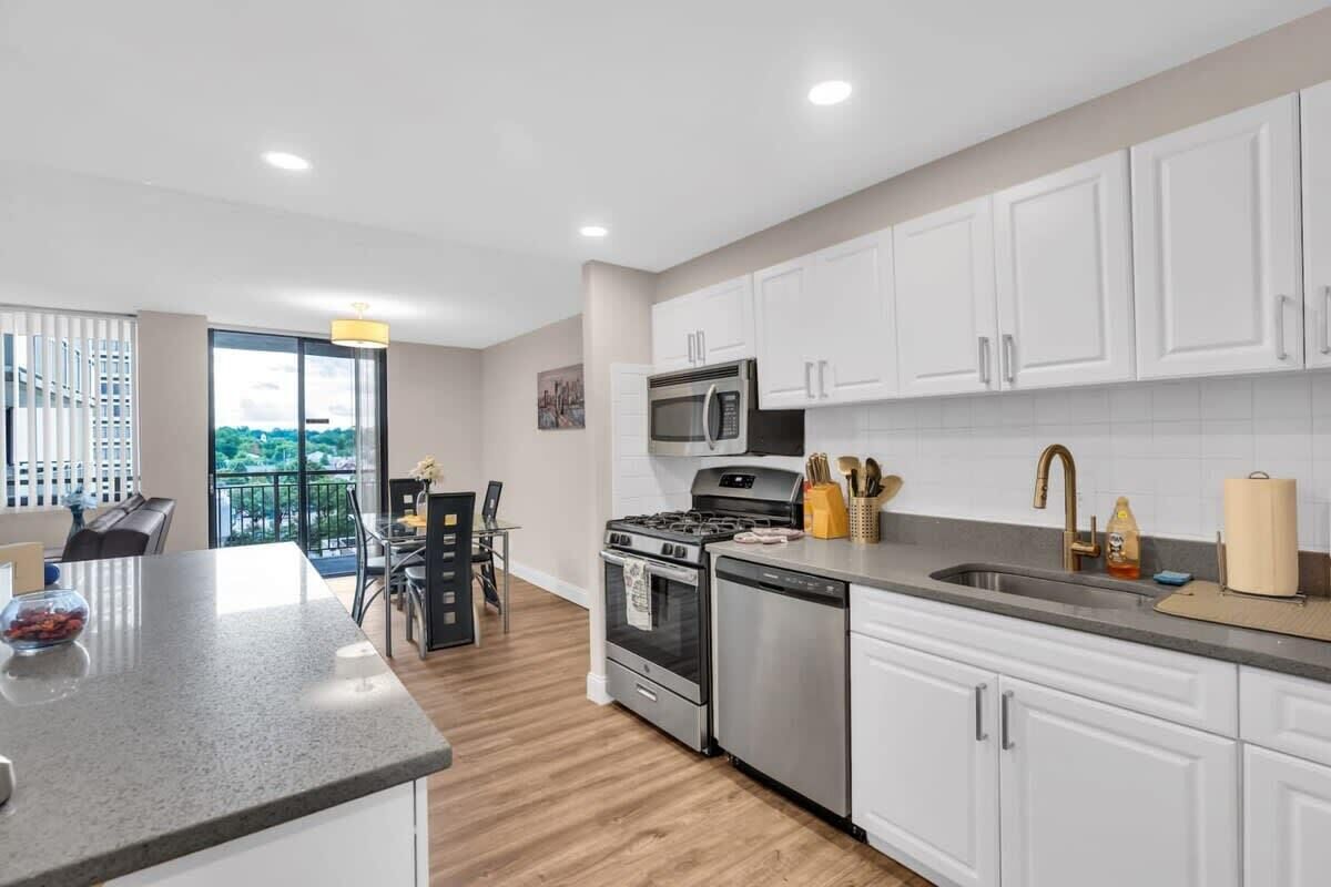 A modern kitchen with white cabinets, stainless steel appliances, and a large window overlooking a balcony.