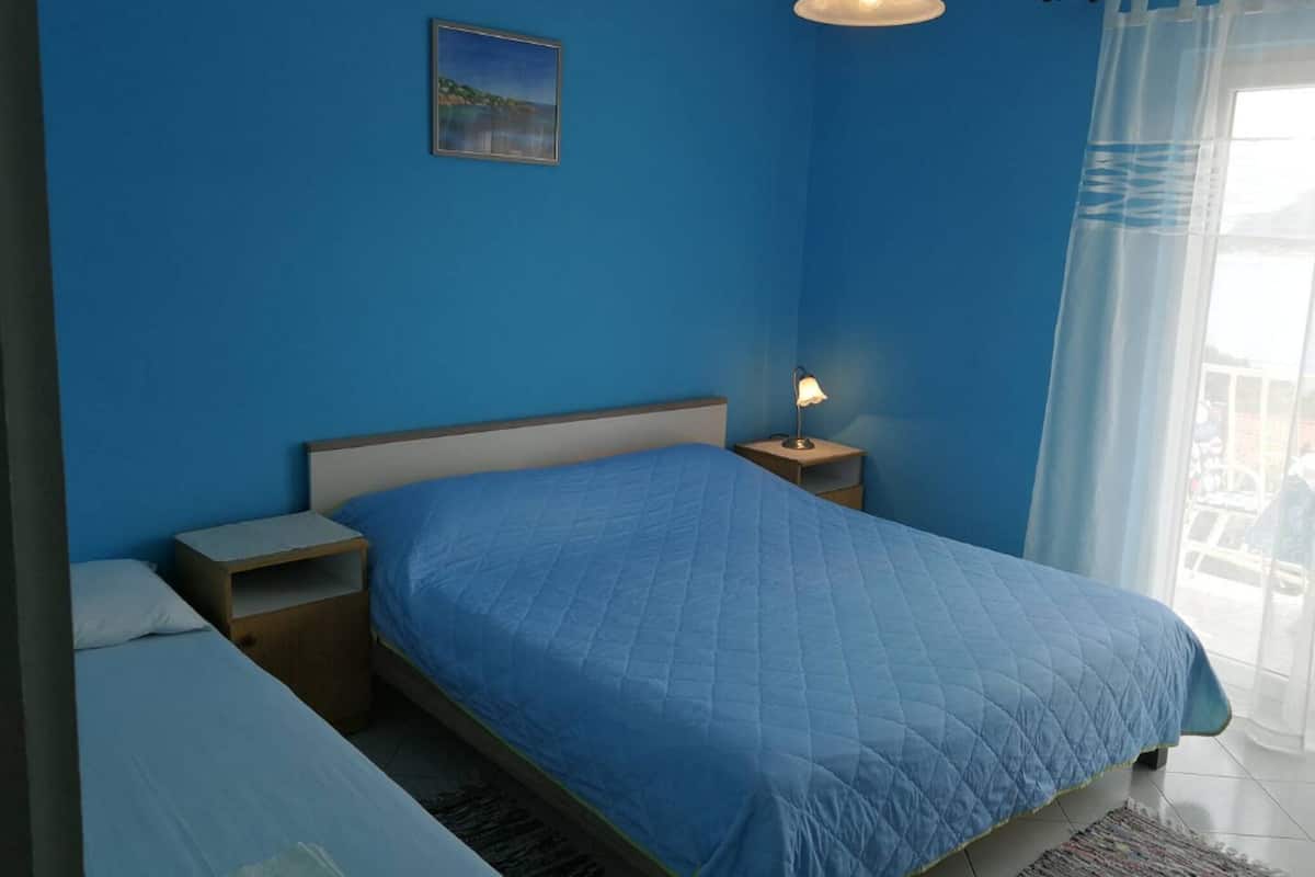 Ein Schlafzimmer mit einem Einzelbett, einem Nachttisch, einer Nachttischlampe, einem Bild an der Wand und einem Fenster mit Vorhängen.
