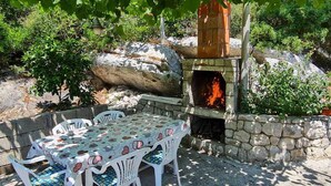 Un espacio al aire libre para comer con un horno de pizza de piedra, rodeado de vegetación y un rústico muro de piedra.