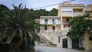 Un edificio de dos pisos con una escalera de piedra que conduce al nivel superior, rodeado de vegetación y una palmera.