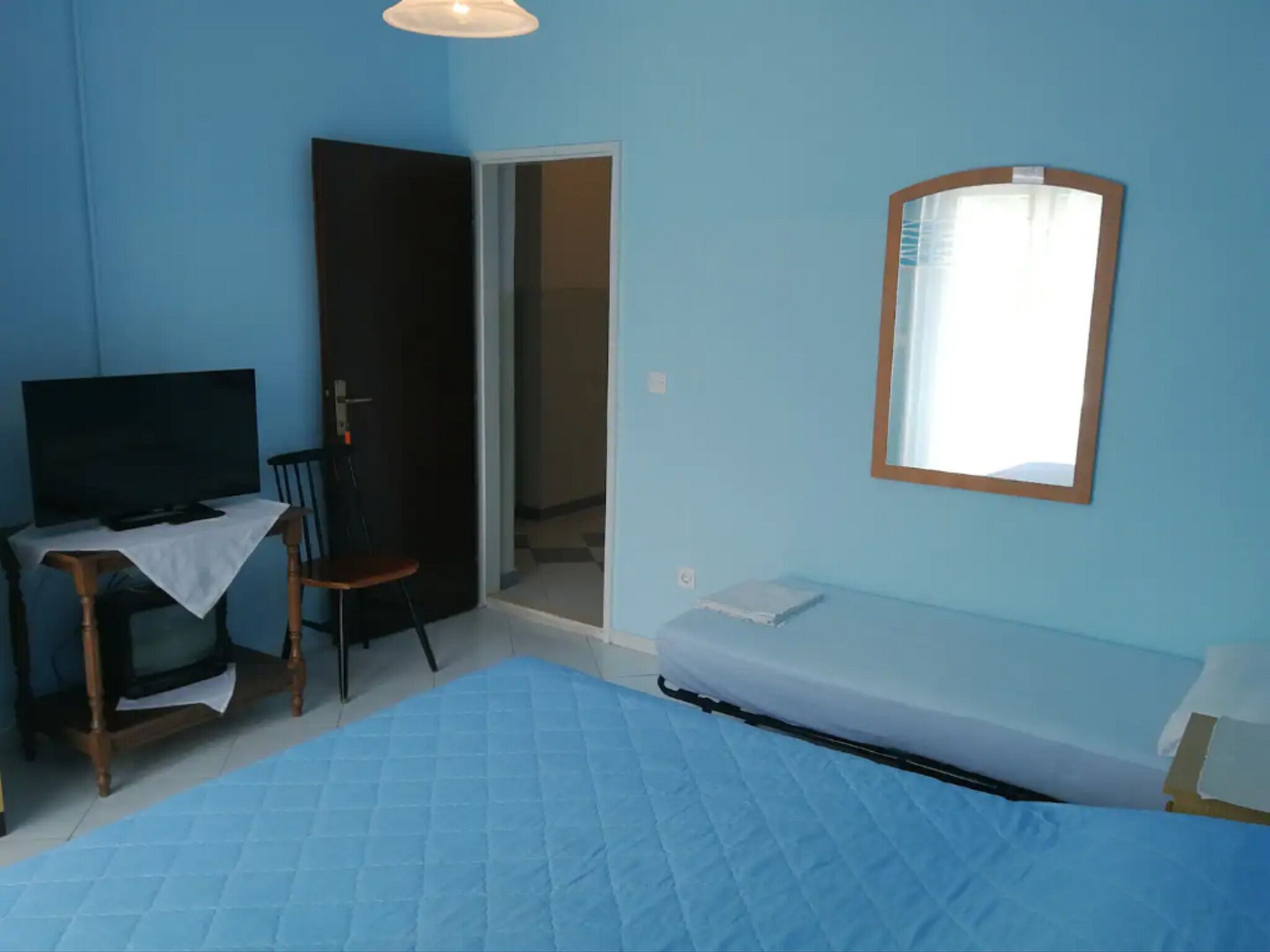 Una habitación con una cama, una silla, un televisor y una puerta que da a otra habitación.