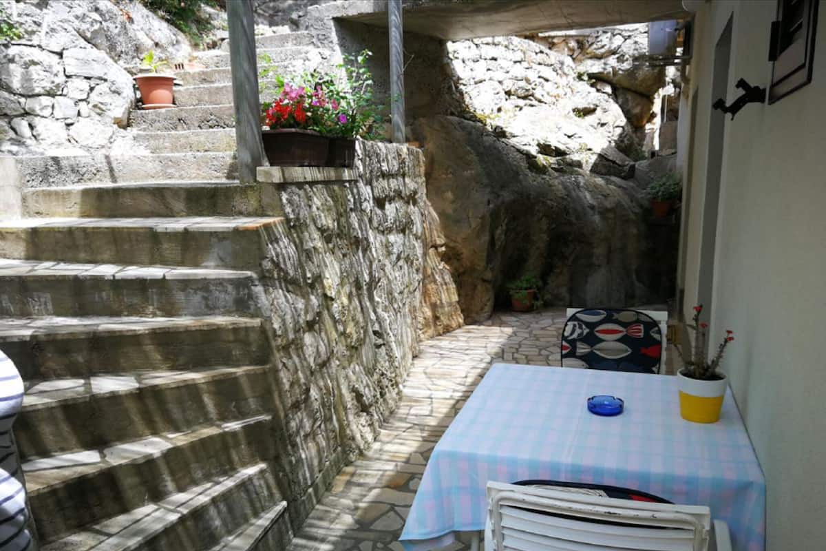 Eine schmale Außenpatio mit Steinstufen, die zu einer Mauer führen, einem Tisch mit kariertem Tischläufer und Blumentöpfen.