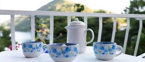 A white table with four cups and a teapot on a balcony with a mountain view.