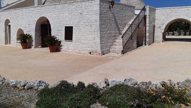 A stone building with multiple arched doorways and a staircase leading to an upper level. - Trulli in Monopolitan countryside  (Puglia)