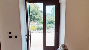 A room with a wooden door leading to an outdoor area, a patterned chair, and a small rug on the floor. - Trulli in Monopolitan countryside  (Puglia)