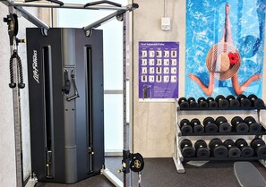 Ein Fitnessstudio mit Kabelzugmaschine, einem Poster einer Schwimmerin und einem Hantelgestell.